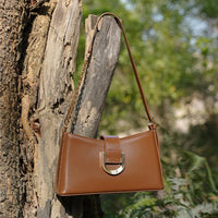 Brown leather handbag with gold buckle on tree outdoors, stylish purse fashion accessory