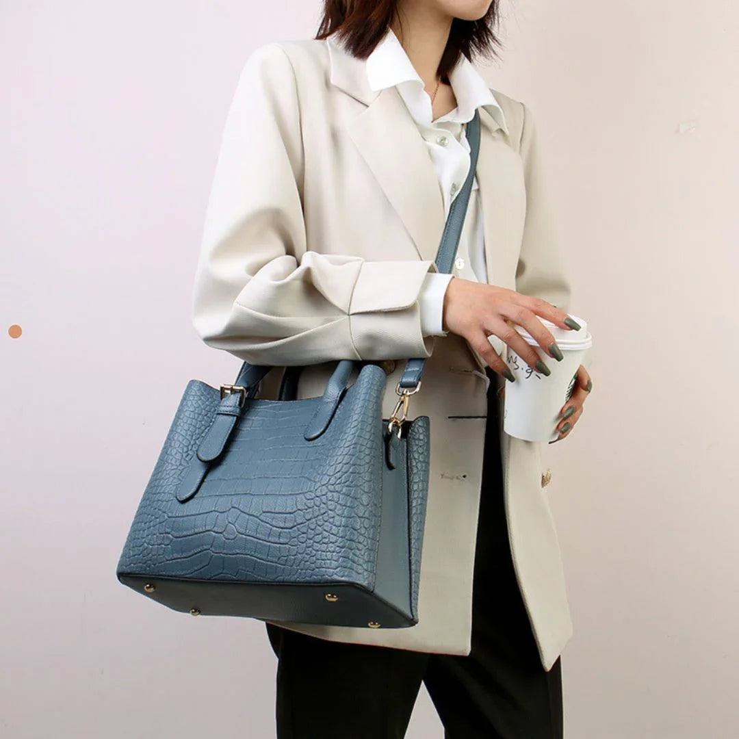 Woman in beige blazer holding coffee cup, wearing stylish blue crocodile pattern handbag