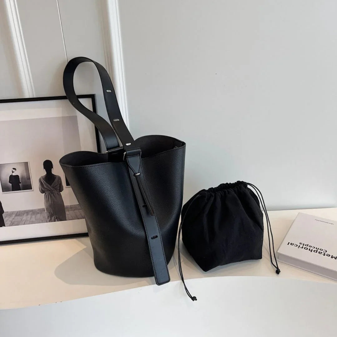 Black leather bucket bag with drawstring pouch on white table, minimalist decor