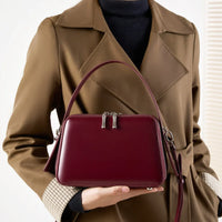 Woman in brown trench coat holding burgundy leather handbag with top handle