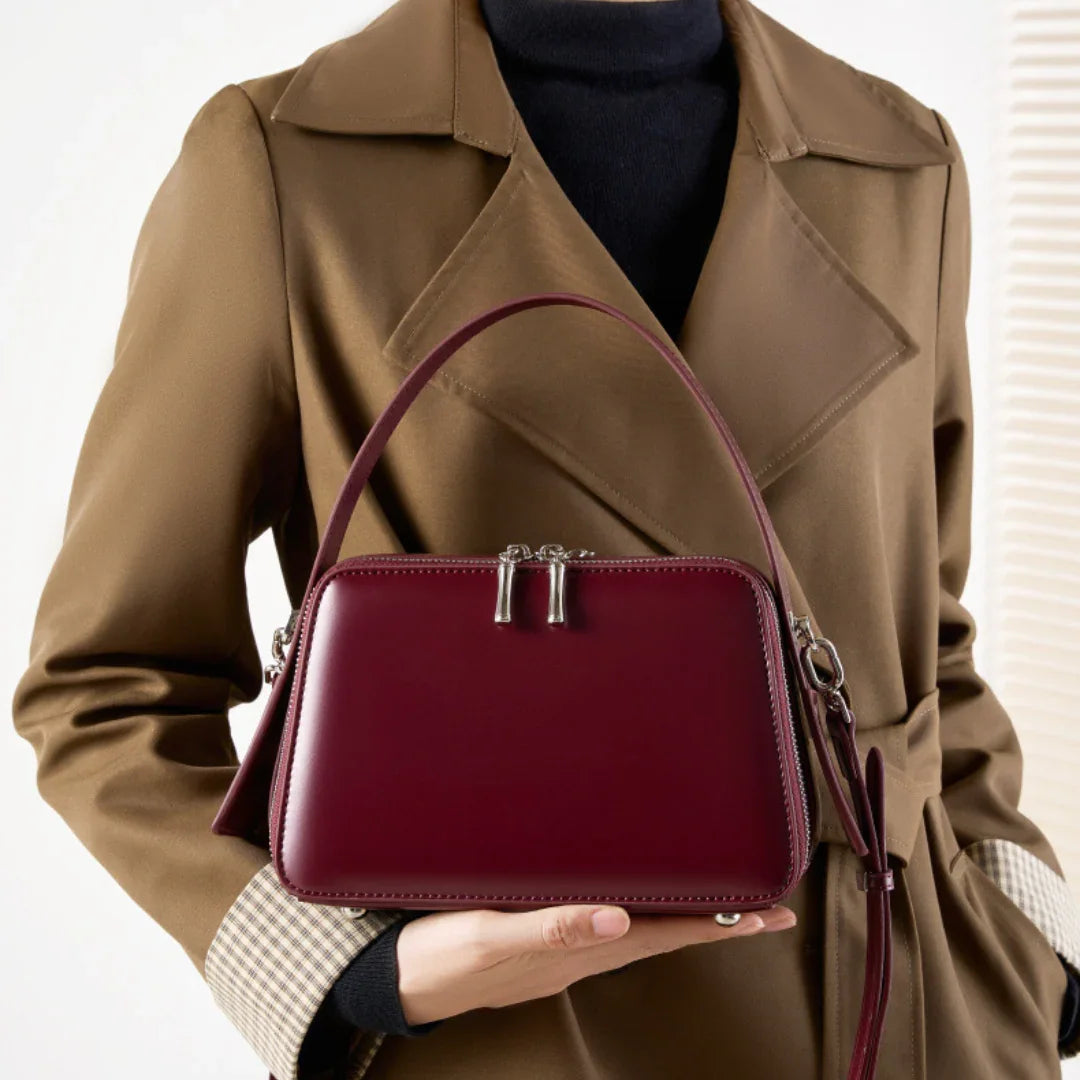 Woman in brown trench coat holding burgundy leather handbag with top handle