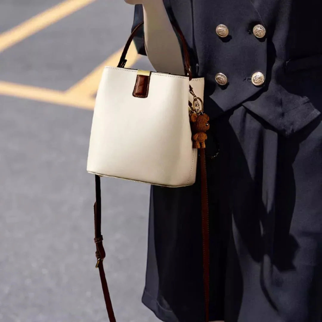White leather handbag with brown handle and bear charm, held by person in navy coat