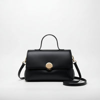 Black leather handbag with gold clasp, top handle, and shoulder strap on white background
