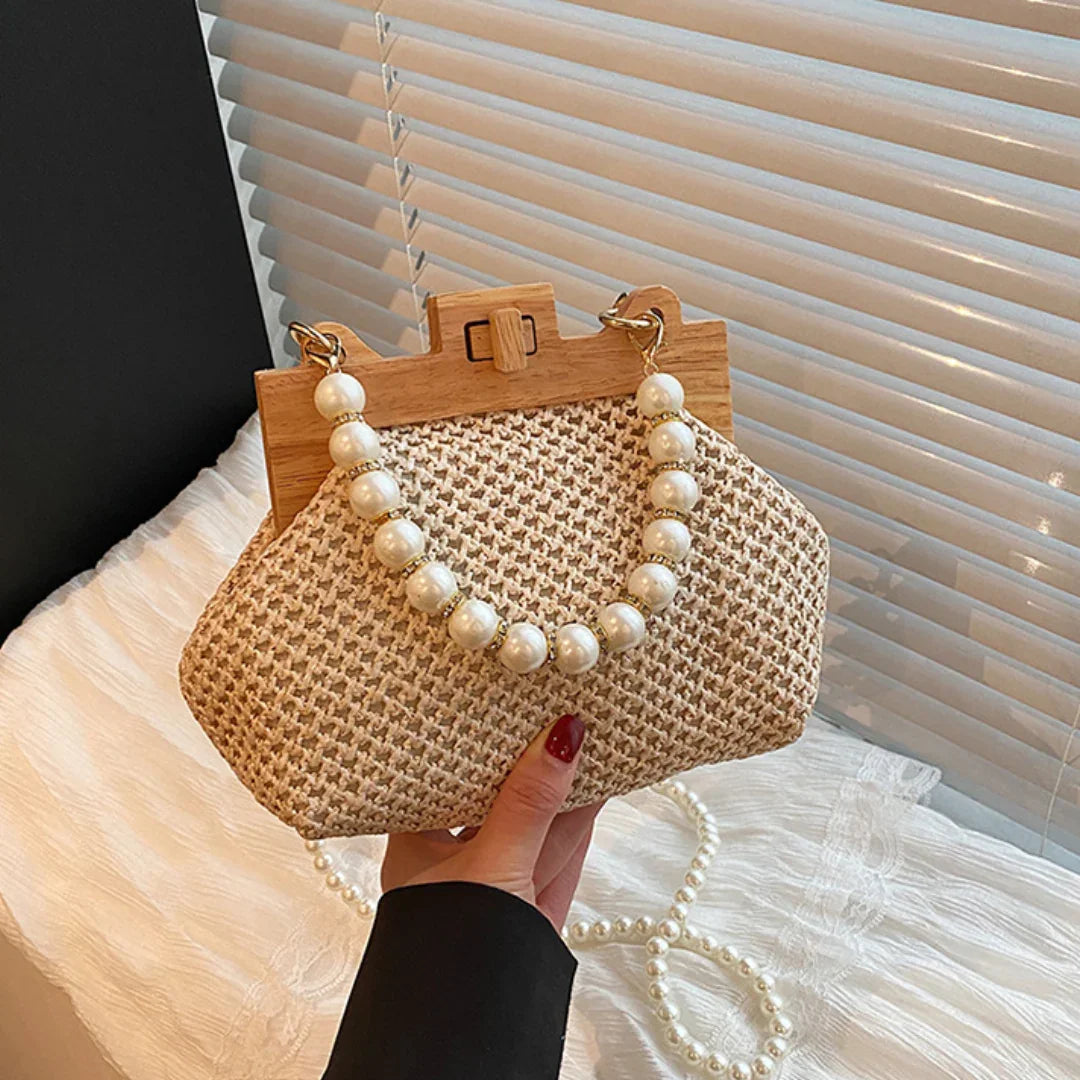Woven straw handbag with pearl handle and wooden frame, held by hand near window blinds