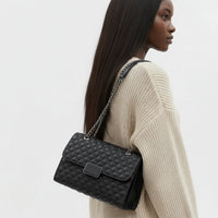 Woman wearing cream sweater with black quilted leather shoulder bag and chain strap