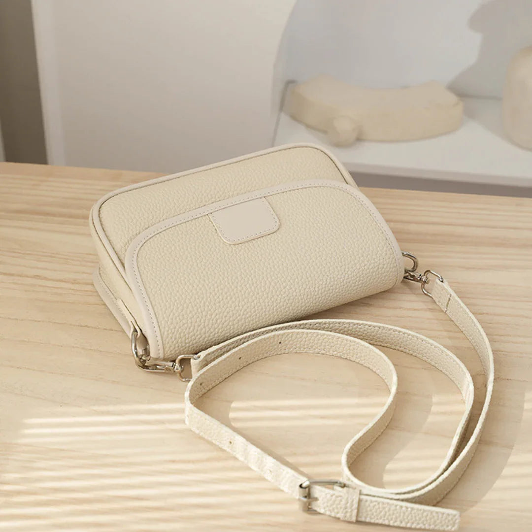 Beige leather crossbody bag on light wooden table in minimalist setting