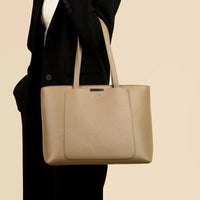 Beige leather tote bag on woman in black blazer against neutral background