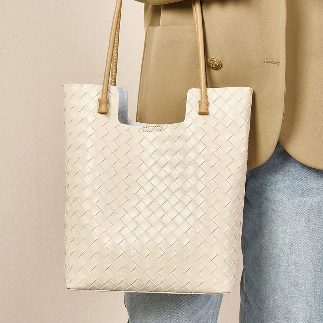 Beige woven leather tote bag with tan handles, styled with a tan blazer and blue jeans