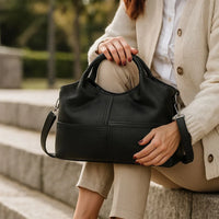 Woman sitting outdoors holding a large black leather handbag on stone steps