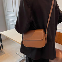 Woman in black blazer wearing a brown leather crossbody bag in modern office setting