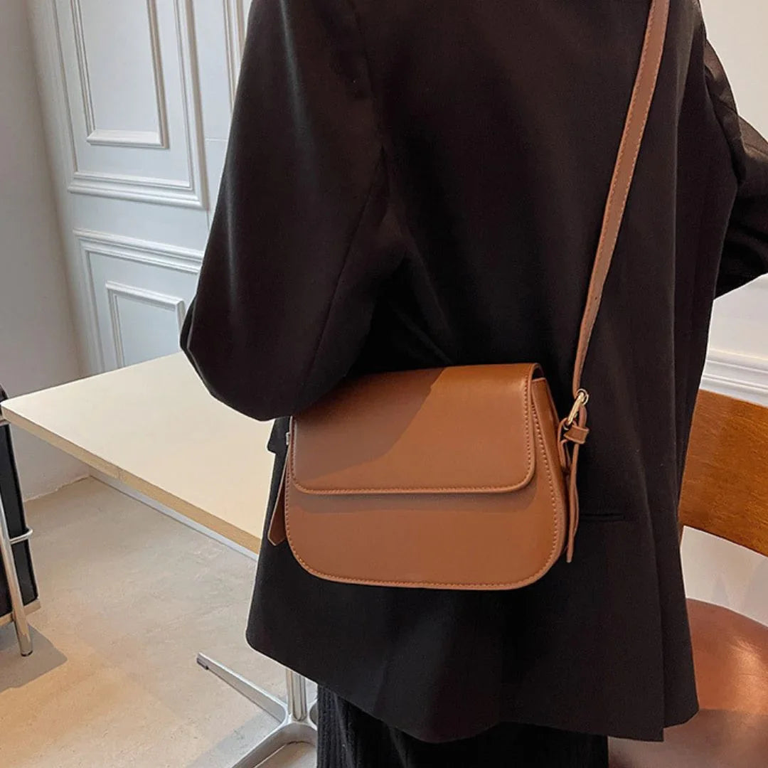 Woman in black blazer wearing a brown leather crossbody bag in modern office setting