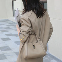 Woman in tan blazer with gold buttons holding magazine and taupe leather handbag outdoors