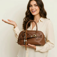 Woman in cream blouse holding brown leather handbag with gold hardware and decorative charms