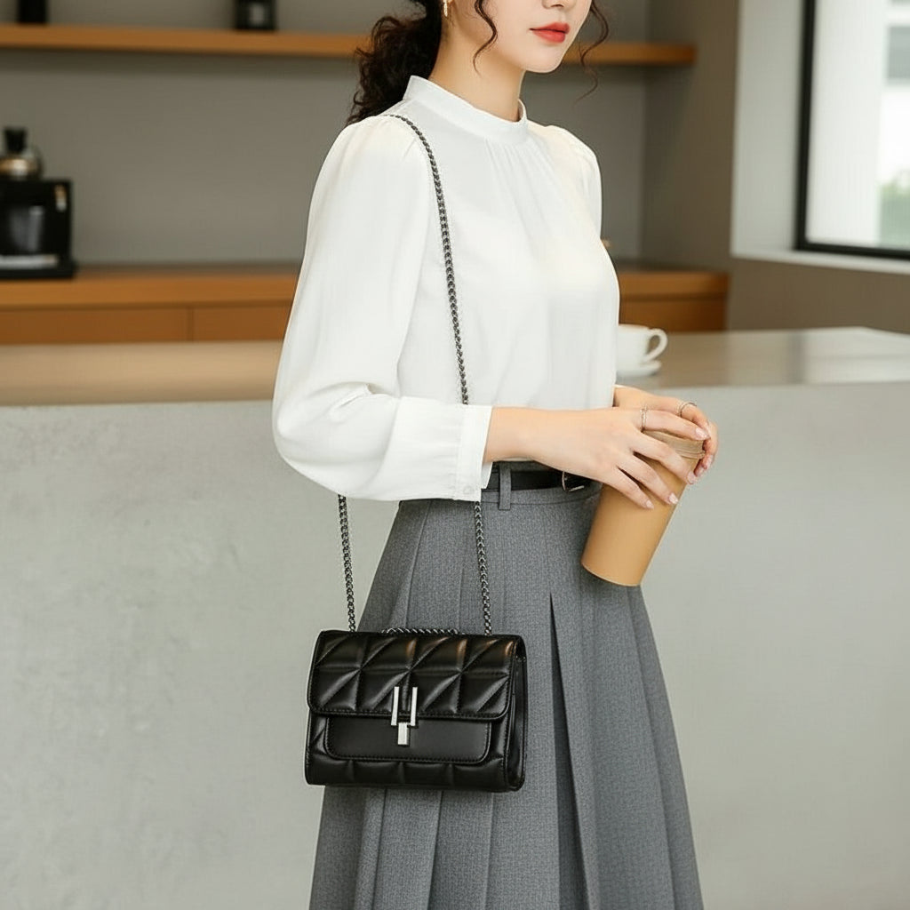 Woman in white blouse and gray skirt with black quilted purse holding coffee cup indoors