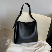 Black leather tote bag with adjustable strap on a cream chair