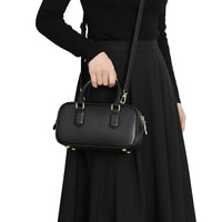 Woman in black dress holding a small black leather handbag with gold accents