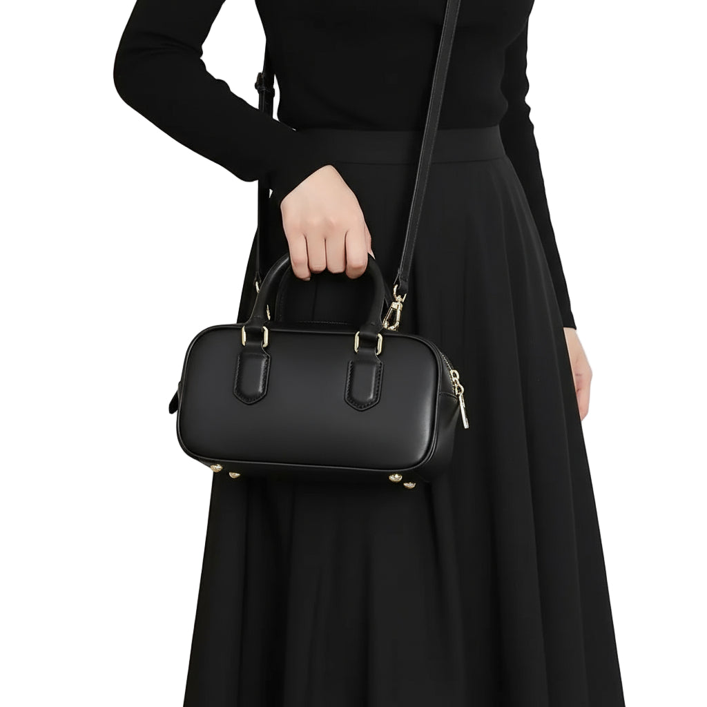 Woman in black dress holding a small black leather handbag with gold accents