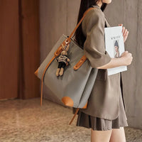 Woman holding magazine, wearing brown outfit and gray tote bag with leather straps and doll keychain