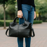 Woman holding black leather handbag outdoors, wearing blue jeans and black sweater