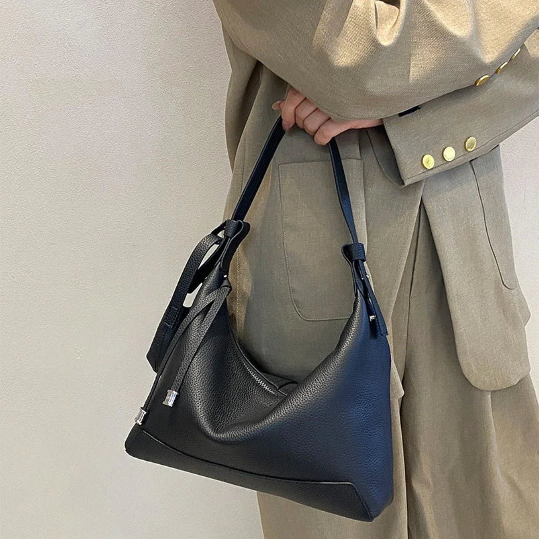 Woman in beige suit holding black leather shoulder bag with knot detail