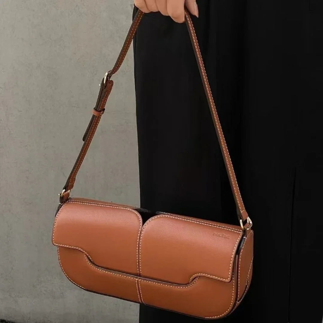 Woman holding brown leather shoulder bag with white stitching against black dress