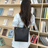 Woman with long hair and black quilted shoulder bag in front of bookshelf