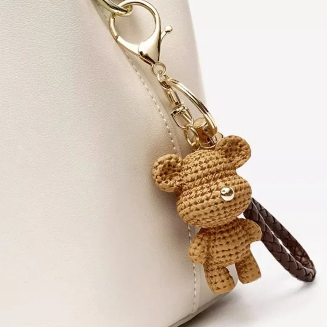 Woven bear keychain on cream handbag with gold clasp and brown leather strap
