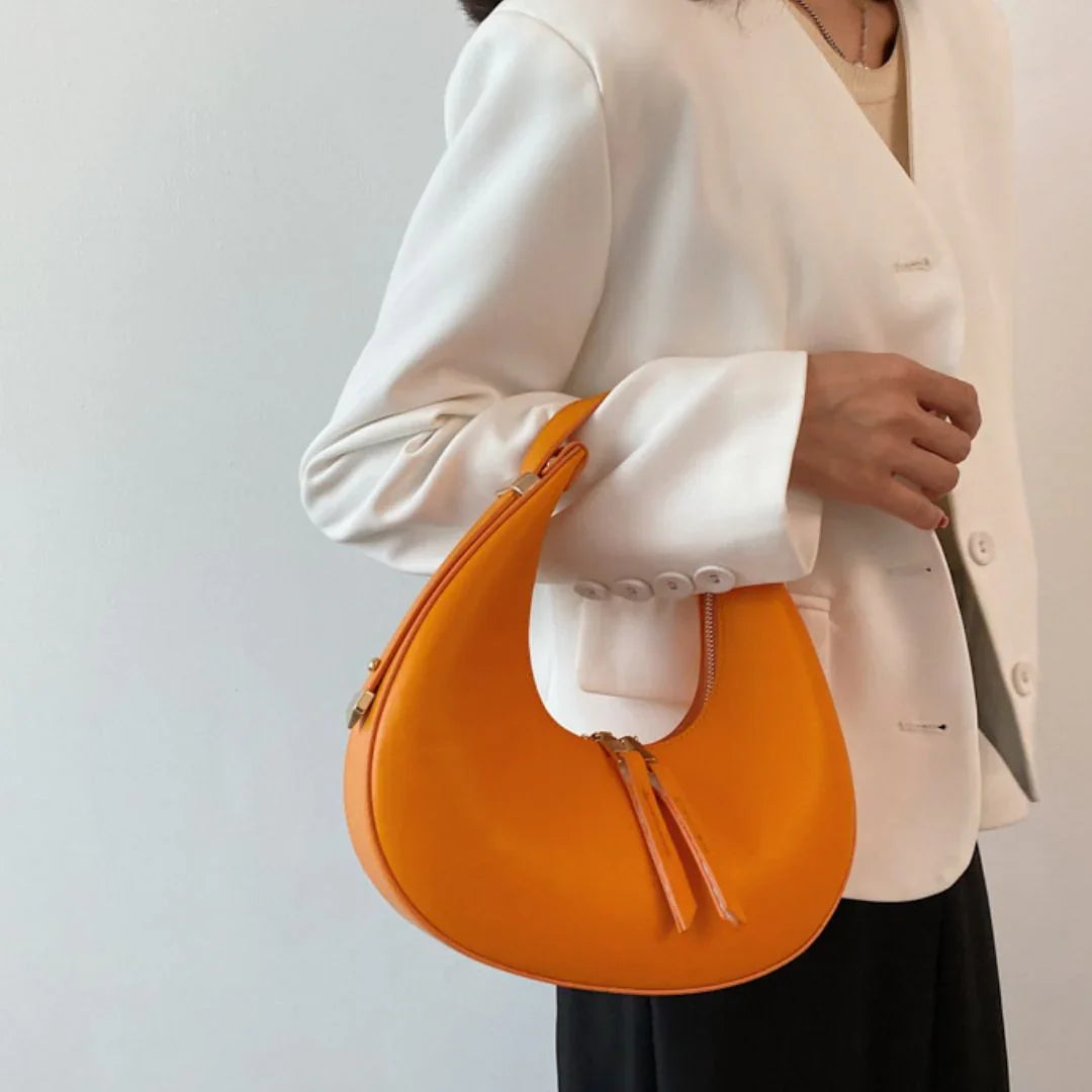 Woman in white blazer holding crescent-shaped orange handbag, minimalist fashion style