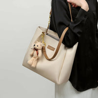 Beige tote bag with brown handles, bear keychain, CLASSIC label, worn by woman in black shirt