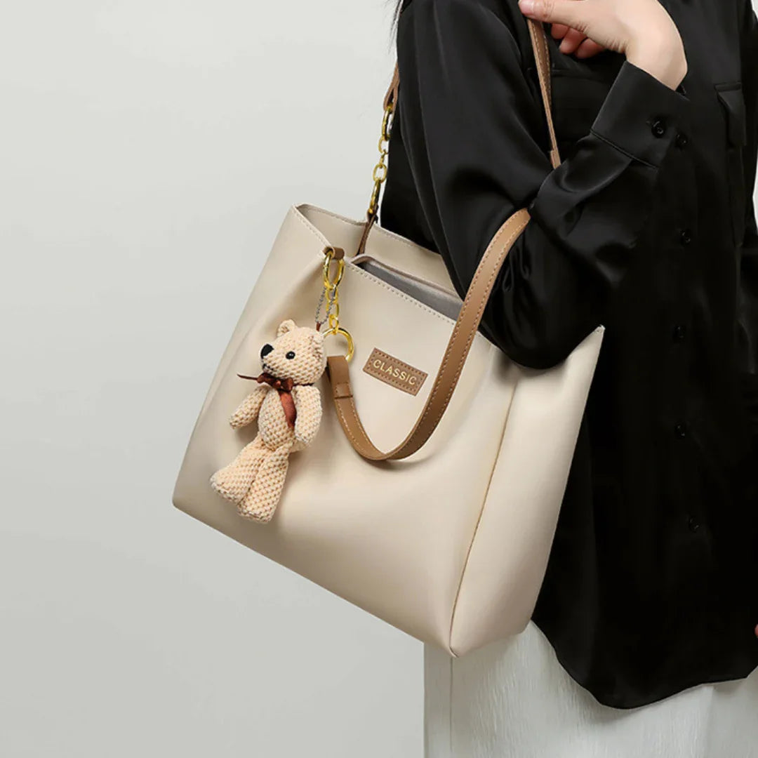 Beige tote bag with brown handles, bear keychain, CLASSIC label, worn by woman in black shirt