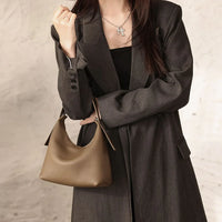 Woman in dark blazer holding brown leather shoulder bag, minimalist fashion style