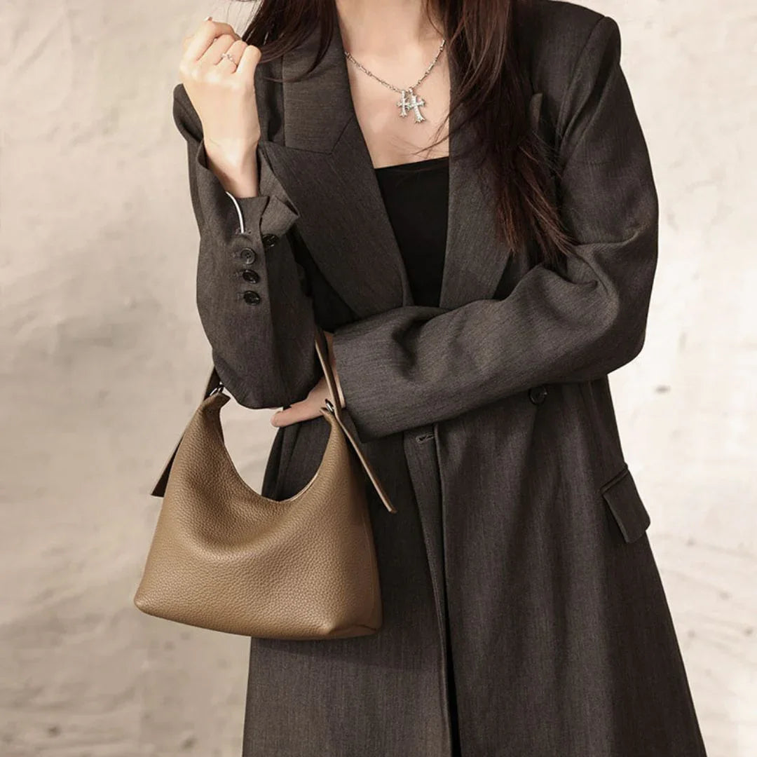 Woman in dark blazer holding brown leather shoulder bag, minimalist fashion style