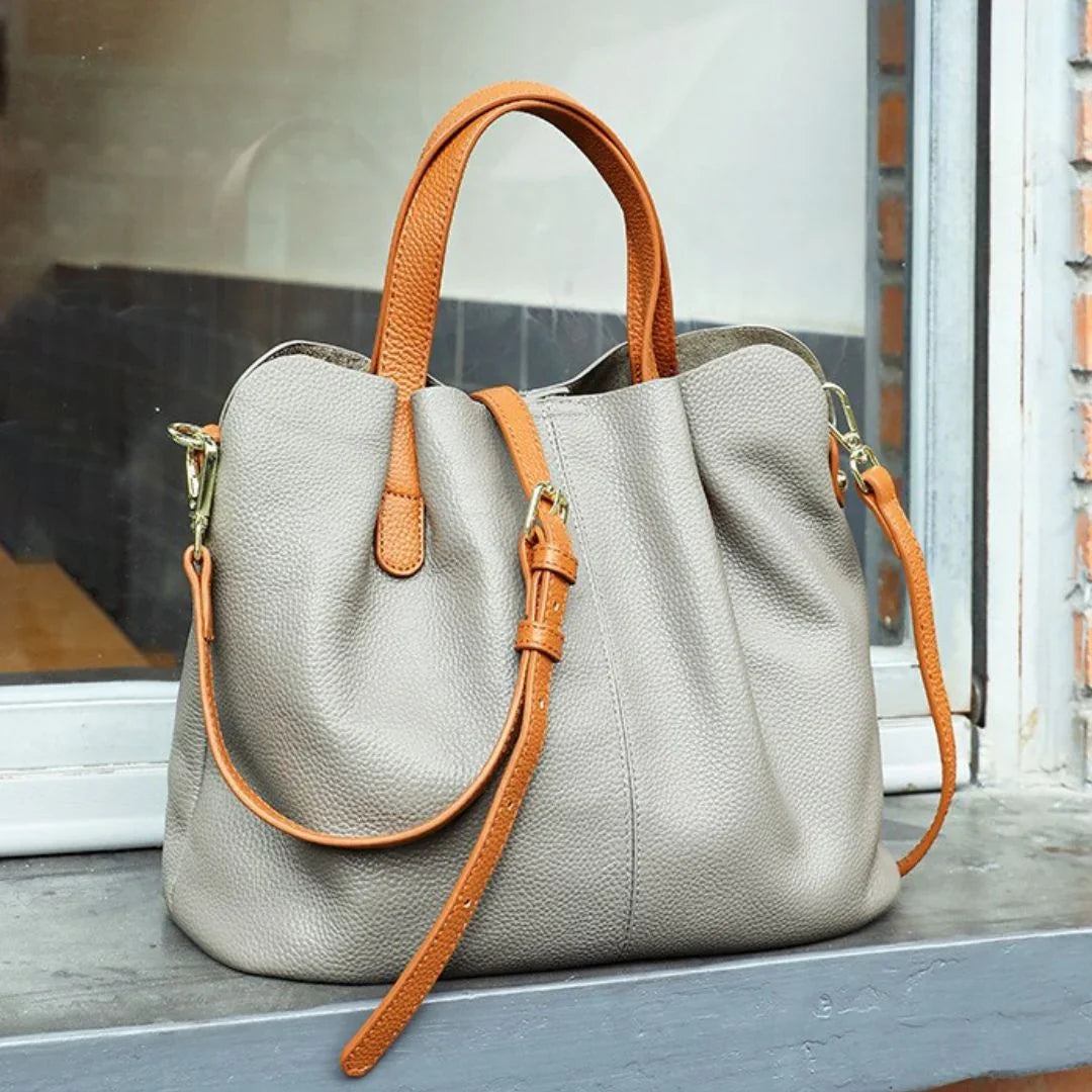 Taupe leather handbag with tan straps on windowsill, stylish women's purse