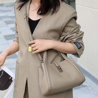 Woman wearing beige blazer and holding taupe leather handbag on city sidewalk