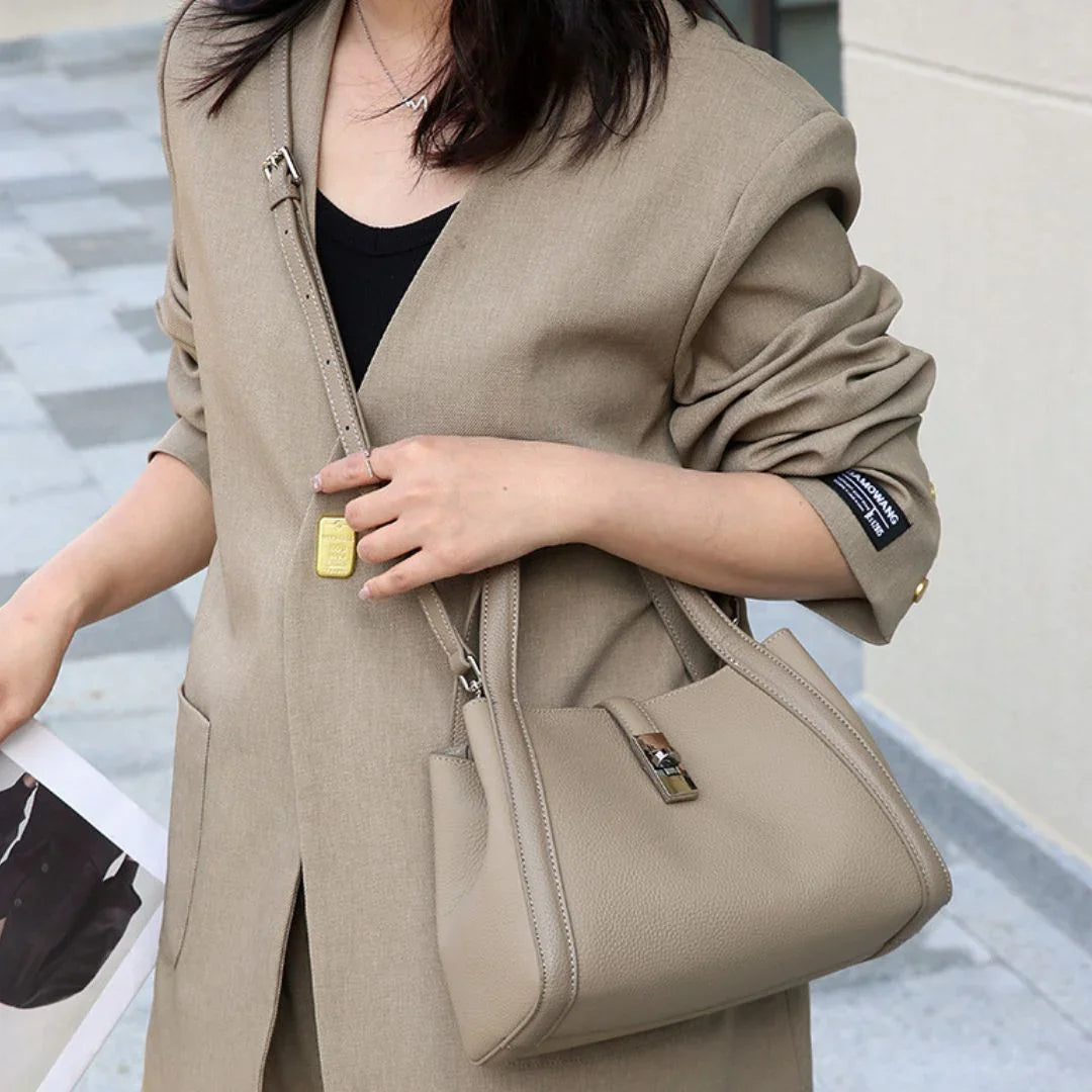 Woman wearing beige blazer and holding taupe leather handbag on city sidewalk