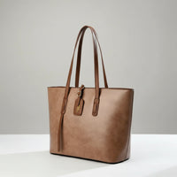 Brown leather tote bag with double handles on a white table, minimalist background