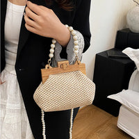 Woman holding woven straw handbag with pearl handle, wearing black blazer indoors