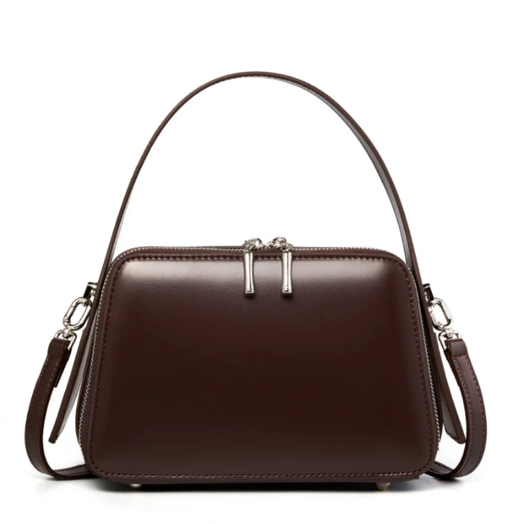 Brown leather handbag with double zipper, top handle, and shoulder strap on white background