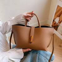 Woman holding stylish brown leather handbag with gold accent and textured surface