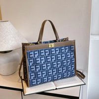 Blue patterned tote bag with brown leather trim on an open book beside a table lamp