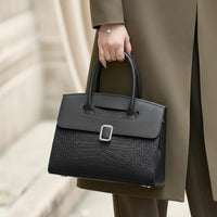 Woman holding black crocodile-embossed leather handbag with silver buckle, outdoor fashion