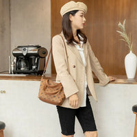 Woman in beige blazer and beret with brown handbag at coffee bar counter