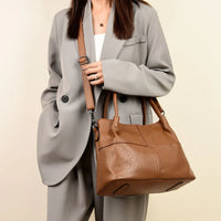Woman in grey suit carrying a brown leather shoulder bag with top handles
