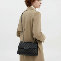 Woman in beige coat with black quilted leather shoulder bag and chain strap