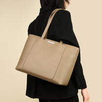 Woman in black blazer carrying taupe leather tote bag on shoulder