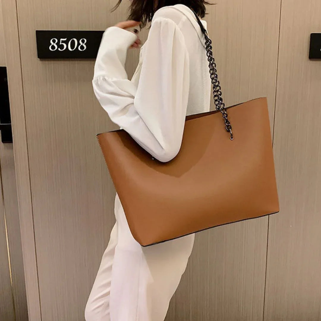 Woman in white outfit holding large brown leather tote bag with chain strap by hotel door 8508