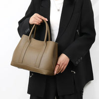 Woman in black blazer holding a large taupe leather handbag against white background