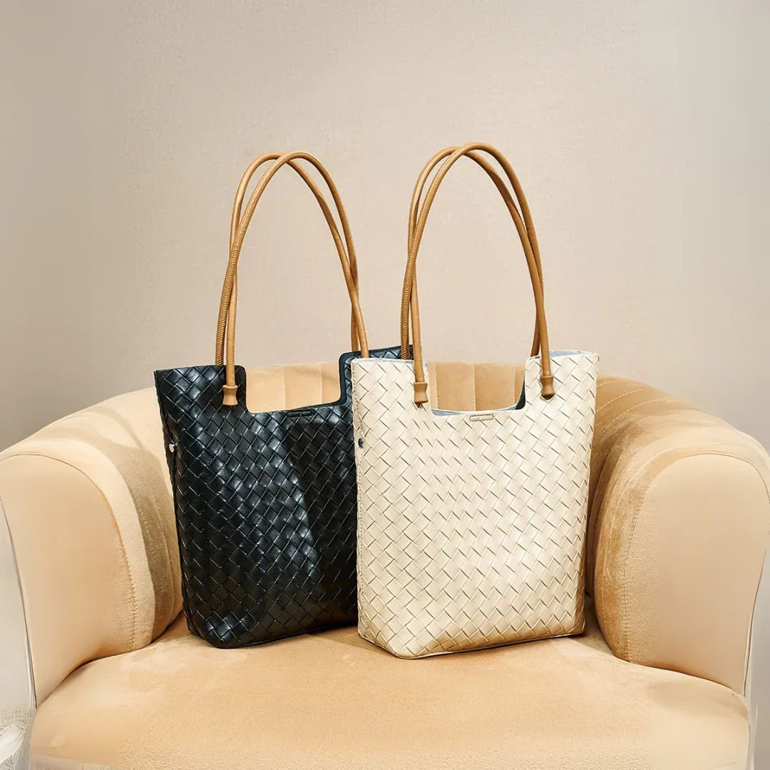 Black and white woven leather tote bags with brown handles on beige chair