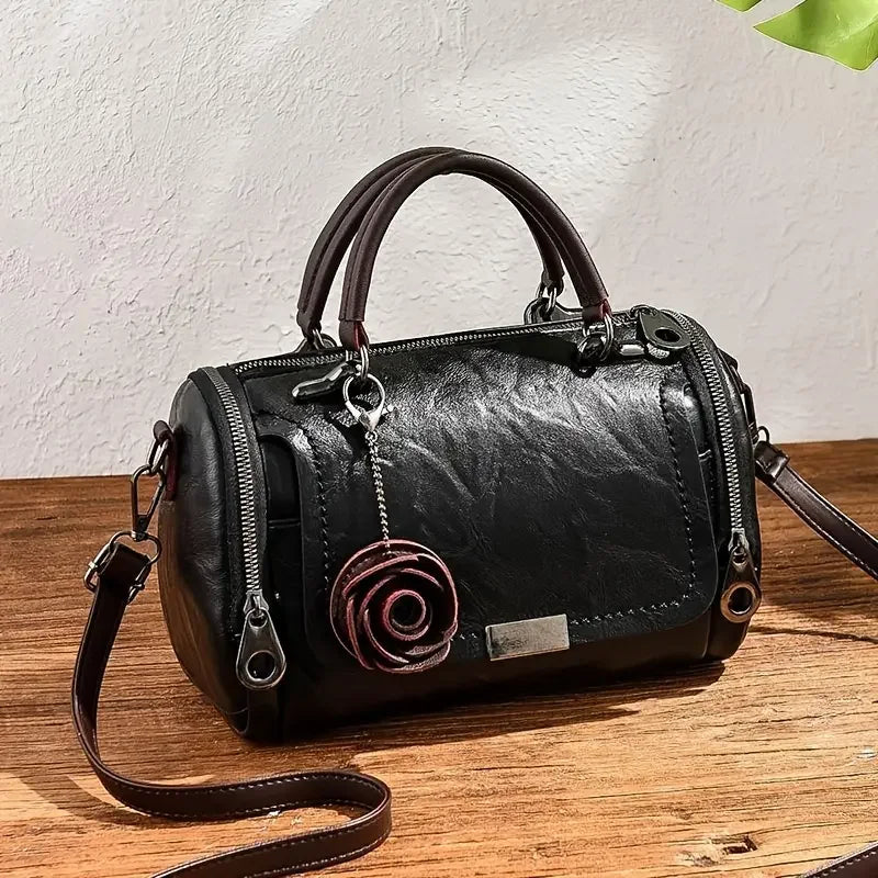 Black leather handbag with rose charm, top handles, and shoulder strap on wood table