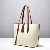 Cream tote bag with brown leather straps on white surface, minimalist handbag